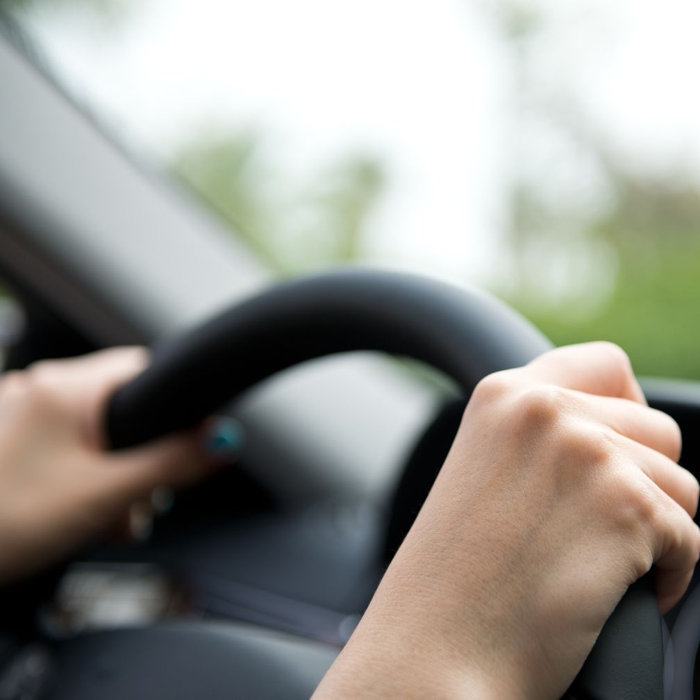 Close-up of a persons hands gripping a steering wheel inside a car, with the background blurred, suggesting motion or focus on driving.