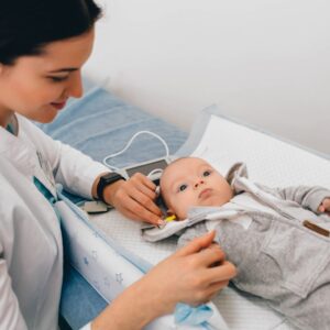 A healthcare professional tests a babys hearing using specialized equipment while the baby lies on an examination table in a clinic.