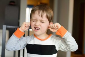 A young boy with his eyes closed and mouth open, plugging both ears with his fingers.